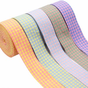 Peut inclure: Un rouleau de ruban en tissu présentant un motif à carreaux vichy répété dans plusieurs couleurs pastel, notamment jaune, bleu clair, violet clair, vert et rose. Le ruban est enroulé en une bobine serrée avec plusieurs couches de tissu visibles.