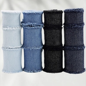Può includere: Quattro pile di tessuto denim in azzurro, blu medio, nero e blu scuro. Ogni pila ha un bordo sfilacciato in alto e in basso, con una forma cilindrica. Il tessuto sembra essere a trama fitta.