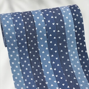 May include: A roll of patterned ribbon in various shades of blue. The ribbon features white star, heart, and floral patterns. The different shades of blue create a visually appealing contrast, ideal for crafting or decorative projects.