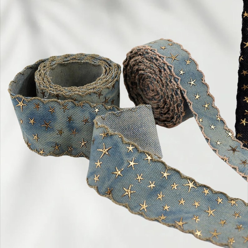 May include: Denim ribbon with gold star embellishments. The ribbon has a scalloped edge and is rolled into several spools. The denim is a light blue color, and the stars are a metallic gold. The ribbon is suitable for crafts and decorations.