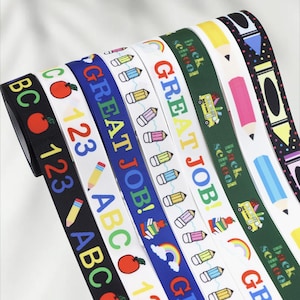 May include: A selection of patterned ribbons with school-related motifs. The ribbons display images of apples, pencils, numbers, and the phrases "GREAT JOB!" and "Back to School". The ribbons are in black, white, blue, and green.