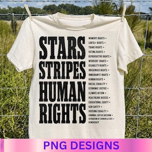 May include: A cream-colored t-shirt featuring large black text that reads STARS STRIPES HUMAN RIGHTS. To the right, a list of social causes is printed in black, including Women's Rights, LGBTQ+ Rights, Voting Rights, and other justice-related topics.