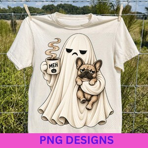 Pode incluir: Uma t-shirt cor de creme com um gráfico de um fantasma com expressão rabugenta segurando uma caneca fumegante com a etiqueta MEH e um ícone de abóbora. O fantasma segura um cachorro buldogue francês castanho. O design usa linhas pretas.