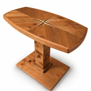 May include: A wooden side table with a compass rose inlay. The table has a rectangular top with rounded corners, supported by a pedestal base. The wood has a warm, natural finish. The table measures approximately 30 inches long.