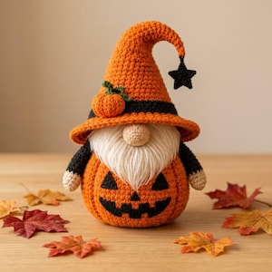 Könnte beinhalten: Eine gehäkelte Zwergenfigur mit einem orangefarbenen, kürbisförmigen Körper und einem schwarzen Jack-o'-Lantern-Gesicht, einem hohen orangefarbenen Hut mit schwarzem Band, einem kleinen Kürbis-Akzent und einem hängenden schwarzen Stern.