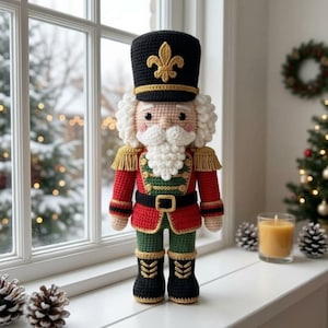 Könnte beinhalten: Eine gehäkelte Nussknacker-Puppe mit einem schwarzen Hut, der ein goldenes Fleur-de-Lis-Emblem trägt, einer roten Jacke mit grünen Akzenten und goldenen Fransen-Epauletten, einem weißen Bart und schwarzen Stiefeln. Die Puppe hat einen Gürtel.