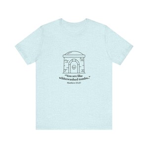 Puede incluir: Camiseta azul claro con un dibujo lineal negro de una tumba y una calavera, y el texto "Sois como sepulcros blanqueados.." Mateo 23:27. La camiseta está hecha de un material suave y cómodo.