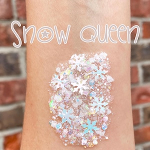 May include: A swatch of clear gel containing iridescent white glitter and small white snowflake-shaped sequins applied to skin. The text "Snow queen" is written in a white, stylized font above the glittery gel application.