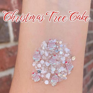May include: A cosmetic glitter gel featuring small, light green and red striped Christmas tree-shaped confetti pieces mixed with iridescent white and silver hexagonal glitter particles. The text Christmas Tree Cake is displayed above.