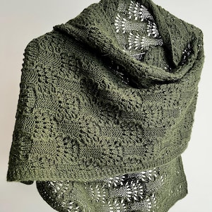 May include: Olive green knitted shawl with a hood. The shawl features a textured pattern and a delicate openwork design on the lower edge. The garment is displayed on a hanger against a white background.