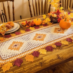 Pode incluir: Uma mesa de jantar de madeira está decorada para o outono com um caminho de mesa de crochê com padrões florais e detalhes de folhas. Abóboras, folhagens de outono e vidraria decorativa completam a exibição sazonal.