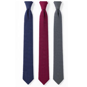 May include: Three textured neckties in a row. The ties are in shades of navy blue, burgundy, and gray. Each tie has a woven, waffle-like pattern. The ties are displayed against a white background.