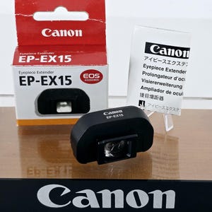 May include: A black Canon EP-EX15 eyepiece extender for cameras, positioned in front of its original red and white cardboard packaging box and a white instruction manual featuring the Canon logo and multi-language product text.