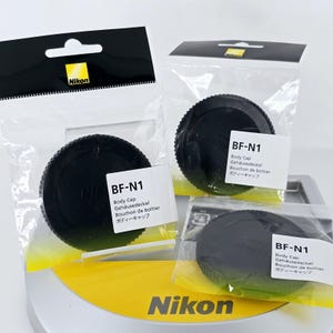 May include: Three black Nikon BF-N1 body caps, each individually sealed in clear plastic packaging with a white label. The labels feature the text BF-N1, Body Cap, Gehäusedeckel, Bouchon de boîtier, and Japanese characters for body cap.
