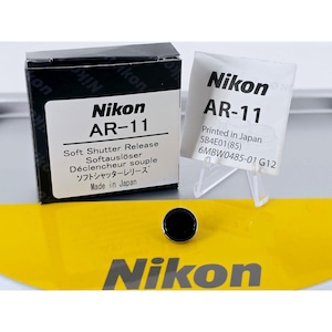 May include: A black Nikon AR-11 soft shutter release button positioned in front of its black and white product box and a small instruction manual. The box features the text Nikon AR-11 Soft Shutter Release and Made in Japan clearly printed.