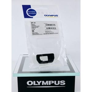 Może przedstawiać: Muszla oczna Olympus EP-16 zapakowana w przezroczystą plastikową torebkę z białą kartą nagłówkową. Etykieta zawiera nazwę produktu, kody kreskowe oraz informacje o producencie. Czarna muszla oczna jest widoczna przez opakowanie.
