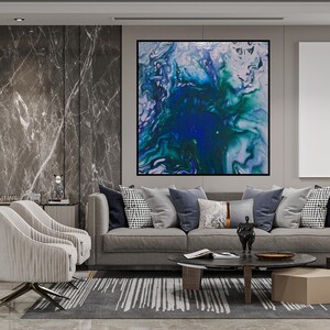 May include: An abstract painting with a black frame, featuring swirling patterns of blue, green, and white. The artwork hangs above a gray sofa adorned with various pillows. The room includes two armchairs, a coffee table, and a patterned rug.