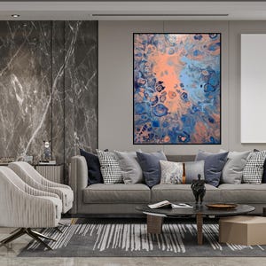 May include: Abstract art piece in a black frame, featuring a blend of coral, blue, and navy hues. The artwork is displayed above a gray sofa with various throw pillows. The room has a modern, minimalist design.