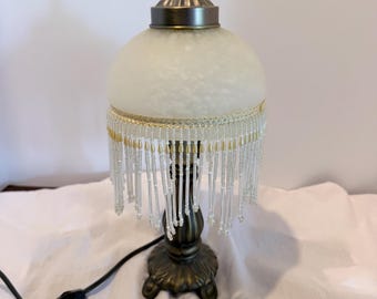 Victorian-style boudoir table lamp features an ornate antique bronze base and a mottled glass dome shade with fringe/beading to lamp shade