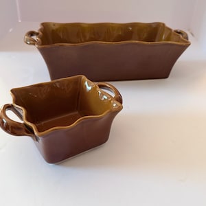 May include: A rectangular brown ceramic baking dish and a smaller square brown ceramic baking dish. Both vessels feature a glossy finish, wavy scalloped edges along the top rim, and small integrated handles on opposite sides for easy gripping.