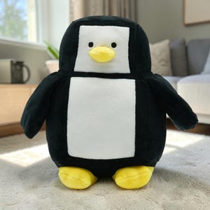 以下が含まれることがあります： 黒い体、白い胸、黄色い足とくちばしを持つ、ぬいぐるみペンギンの玩具。 ペンギンは長方形の白い顔と小さな黒い目を持っています。 おもちゃは白いカーペットの上に立っています。