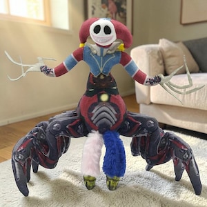 Puede incluir: Una muñeca de peluche con apariencia de payaso. Tiene una cara roja y blanca con ojos negros y una sonrisa cosida. El cuerpo de la muñeca es rojo, azul y negro, con múltiples piernas y brazos. Los brazos tienen extensiones blancas en forma de garra.