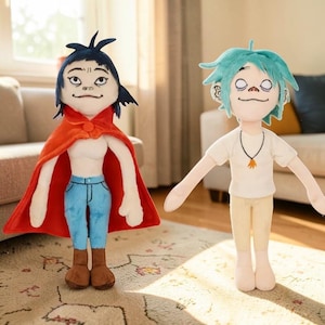 May include: Two plush dolls of cartoon characters. One doll has dark blue hair, a red cape, blue jeans, and brown boots. The other doll has light blue hair, a white shirt, tan pants, and a necklace. Both dolls have detailed facial features.