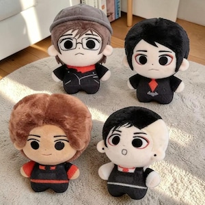 Può includere: Quattro bambole di peluche con facce in stile cartone animato e abiti neri. Le bambole hanno acconciature e accessori diversi, tra cui occhiali e cappelli. Le bambole sono su una superficie chiara e strutturata.