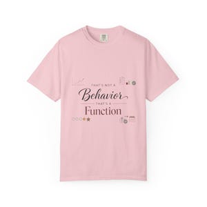 Puede incluir: Camiseta rosa claro con el texto "THAT'S NOT A Behavior THAT'S A Function" en negro. La camiseta presenta pequeños iconos gráficos y es una prenda informal.