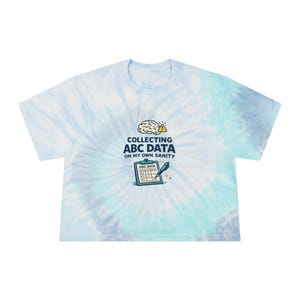May include: A light blue tie-dye crop top with the text "COLLECTING ABC DATA ON MY OWN SANITY". The graphic includes a brain, a clipboard, and a pen. The shirt is a casual, short-sleeved style.