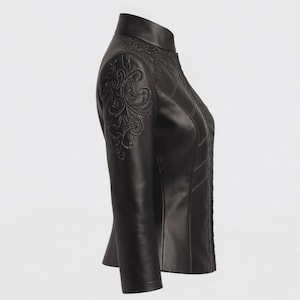 Può includere: Giacca in pelle nera con ricami floreali ornati sulle spalle e sul petto. La giacca presenta un collo alto, una silhouette aderente e dettagli di cucitura decorativi. Un capo di abbigliamento esterno elegante.