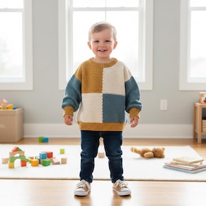 以下が含まれることがあります： パッチワークデザインの子供用手編みかぎ針編みセーター。マスタードイエロー、ティール、クリーム、ネイビーブルーの正方形が特徴です。子供はブルージーンズとタンのスニーカーを履いています。