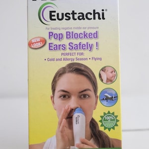 Puede incluir: Una caja para el dispositivo de alivio de la presión del oído NeilMed Eustachi. La caja es blanca, verde y amarilla, con el nombre del producto en letras grandes y en negrita. La caja presenta el texto "Pop Blocked Ears Safely!" e incluye una imagen de una persona usando el dispositivo.