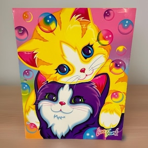 May include: A rectangular Lisa Frank folder featuring a bright yellow kitten with large blue eyes resting above a purple kitten with green eyes. The background is a vibrant pink gradient filled with colorful, translucent floating bubbles.