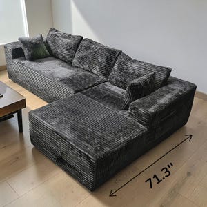 May include: A large, dark gray sectional sofa with a corduroy texture. The sofa has multiple cushions and a chaise lounge section, measuring 71.3 inches in length. The sofa is placed on a light-colored wooden floor.
