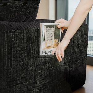 May include: A black corduroy sofa with a magazine in the side pocket. The magazine has the words "live he tran" on the cover. The sofa has a textured, ribbed design.