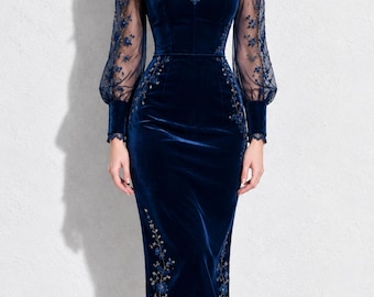 May include: A navy blue velvet midi dress featuring a high neck, sheer long sleeves with floral embroidery, and a sweetheart neckline bodice. The skirt includes matching floral embroidery along the sides and a scalloped lace hemline.