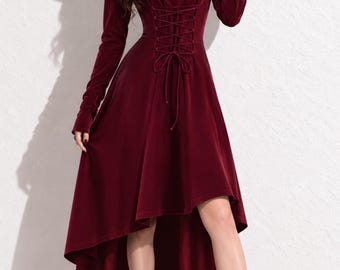 May include: A deep burgundy velvet dress featuring a hood, long sleeves, and a lace-up corset-style bodice. The garment has a high-low hemline that is shorter in the front and longer in the back, paired with matching burgundy high-heeled boots.