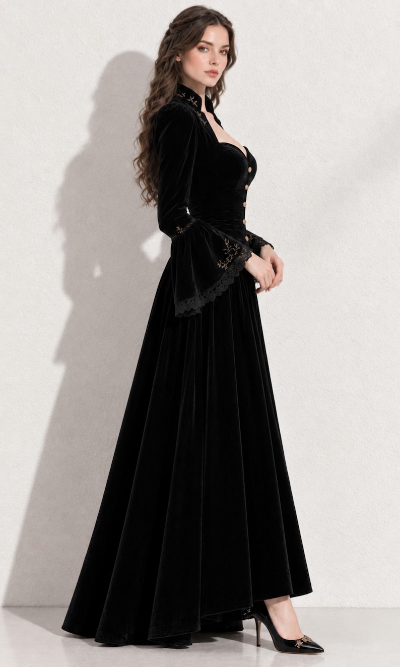 May include: A floor-length black velvet gown featuring a high collar, long sleeves with flared cuffs, and a row of buttons down the front bodice. The garment is accented with delicate gold embroidery along the collar and cuffs, and black lace trim.