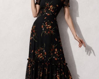 May include: A black midi dress featuring a high neckline and short sleeves with a sheer mesh overlay. The dress is adorned with a vibrant floral print in shades of orange, red, and green, and includes a ruffled hemline at the bottom of the skirt.