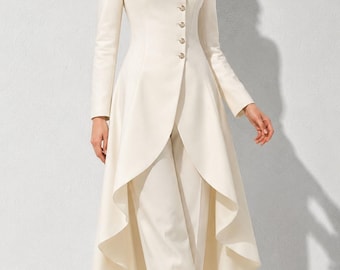 May include: An off-white long-line jacket featuring a mandarin collar, long sleeves, and a side-button closure with metallic buttons. The jacket has a high-low hemline with a dramatic draped back, paired with matching straight-leg trousers and heels.