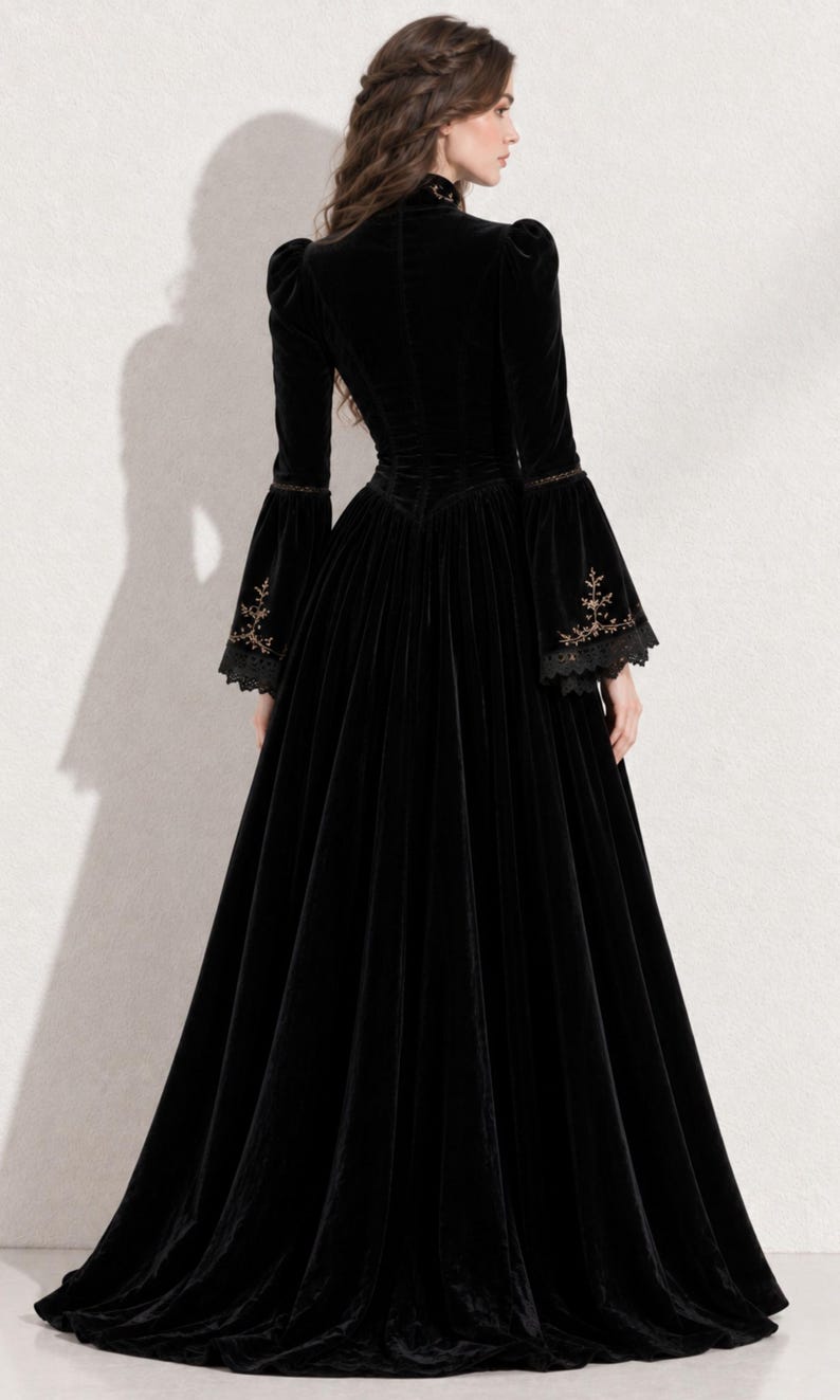 May include: A floor-length black velvet gown featuring a high collar, long sleeves with flared cuffs, and intricate gold embroidery detailing on the lower sleeves. The dress has a fitted bodice and a full, flowing skirt that reaches the floor.