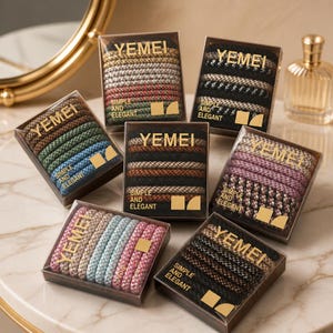 May include: Several boxes of hair ties are shown, each with a collection of elastic bands in different colours and patterns. The boxes are labelled "YEMEI" and "SIMPLE AND ELEGANT". The hair ties are in shades of brown, black, pink, blue, and green.