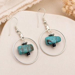 May include: A pair of silver hoop earrings with turquoise and black stone accents. The earrings feature a turquoise stone and a small black bead suspended within a silver hoop. The earrings are designed with a hook closure.