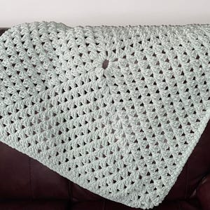 May include: A light green crocheted throw blanket with a square pattern. The blanket is draped over a brown leather couch.
