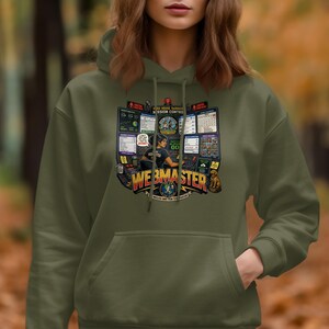 Puede incluir: Una sudadera con capucha de color verde oliva que presenta un estampado gráfico de un centro de control de misión con varias pantallas de ordenador, una persona sentada en un escritorio y el texto "WEBMASTER" en letras amarillas grandes.