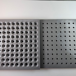 Könnte beinhalten: Zwei quadratische graue Platten nebeneinander. Die linke Platte zeigt ein Raster aus 100 vertieften konischen Einbuchtungen. Die rechte Platte zeigt ein Raster aus 100 kleinen, flachen, kreisförmigen Löchern in einem gleichmäßigen Muster.