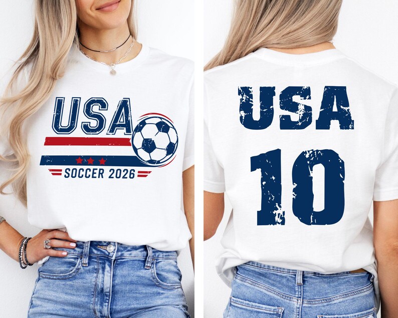 K&ouml;nnte beinhalten: Wei&szlig;es T-Shirt mit "USA SOCCER 2026" Grafik. Das Design auf der Vorderseite zeigt das Wort "USA" in Blau, einen Fu&szlig;ball und rot-blaue Streifen. Auf der R&uuml;ckseite des Shirts stehen "USA" und die Nummer "10" in Blau.