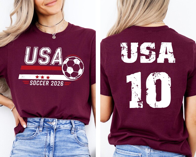 K&ouml;nnte beinhalten: Burgunderfarbenes T-Shirt mit "USA" in Wei&szlig;, einer Fu&szlig;ballgrafik und dem Text "SOCCER 2026". Auf der R&uuml;ckseite des Shirts stehen "USA" und die Nummer "10" in Wei&szlig;.