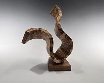 May include: A wooden sculpture with a flowing, abstract design. The sculpture is made of multiple pieces of wood that have been joined together to create a smooth, flowing shape. The sculpture is painted in a natural wood finish.